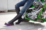 Green motorcycle and a woman in heavy boots near it.